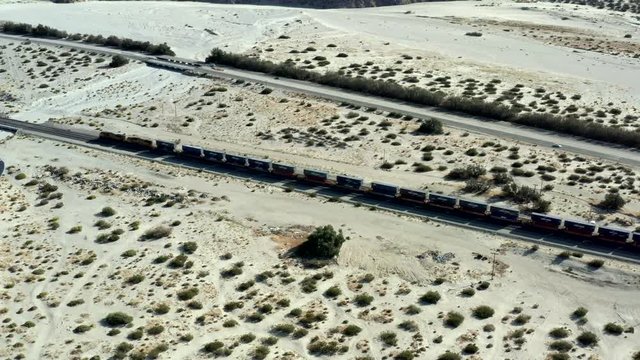 Cinematic Aerial of Cargo Train on Moving on Railway Through Desert on Sunny Day