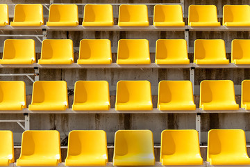 Yellow seats on stands of stadium in open. Rows are horizontal. On seats shade from sun. Front view.