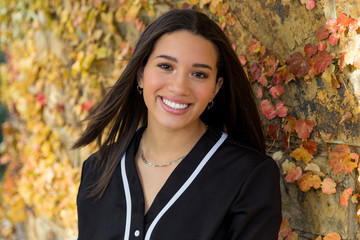 close up of mixed raced teenage girl with fall leaves against a stone wall