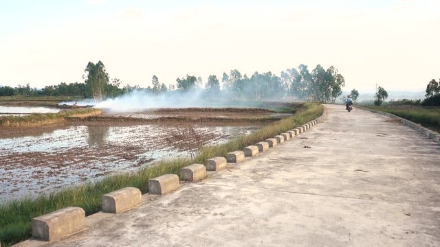 Young Millenial Man on a Scooter on a Empty Road in Vietnam Crossing Smoke from Burning Field