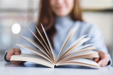 Closeup image of a woman holding and opening a vintage novel book on wooden table