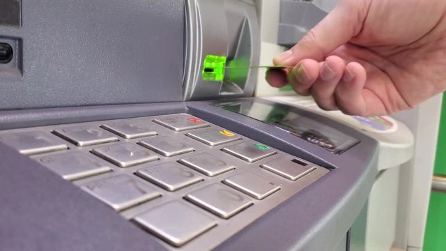 A person making a money withdrawal using debit banking card from ATM machine in the local bank while typing his pin code on the machine keypad