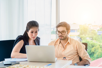 A Businessman and businesswoman looking at laptop computer and paper of work discussing for work diagram in office company with business meeting concept.