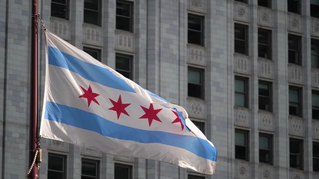 Close up slow motion clip of a Chicago flag flapping and waving in the wind with a highrise building in the background beyond in the city downtown district.
