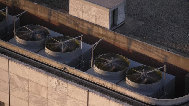 Close up panning aerial view looking down on large rooftop air conditioning unit fans as they run and rotate on a summer day on top of a roof in on a highrise building in downtown Chicago.