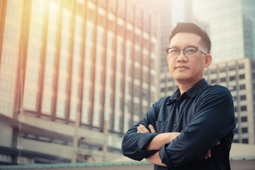Confident male business executive  with arms crossed standing in front of office building
