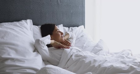 Happy healthy young woman waking up lying in cozy bed