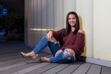 Full length of mixed raced teenage girl sitting next to a white wall smiling