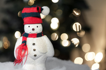 Snowman decoration in snow at night standing in front of distant blurry bokeh lights