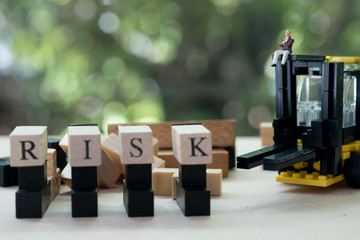 Miniature businessman sitting on forklift with wooden word RISK.  Concept of risk assessment