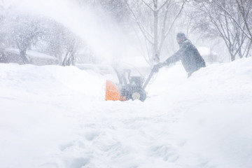 Man using a snowblower to clear his sidewalk and driveway, low visability