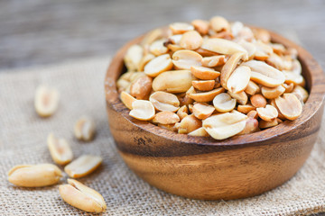 Roasted peanuts on a wooden bowl and sack background - salted peanuts as a food or snack