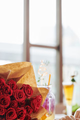 Bouquet of beautiful fresh red roses for woman on table in restaurant with big windows, selective focus