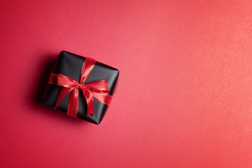 Top view of black gift box with red and black ribbons isolated on red background.