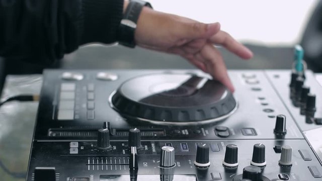 Close up shot DJ hand live perform; turn jog wheel move slidder fadder and switch the knob on dj mixer equipment controller; DJ daytime party
