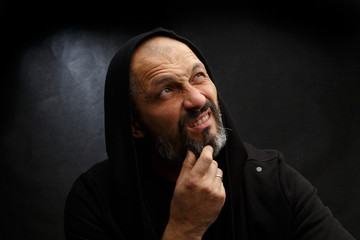 Portrait of a bald man with a beard in a black hood on a dirty gray background.