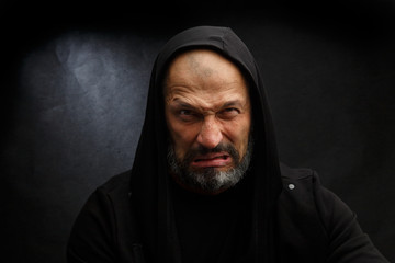 Portrait of a bald man with a beard in a black hood on a dirty gray background.