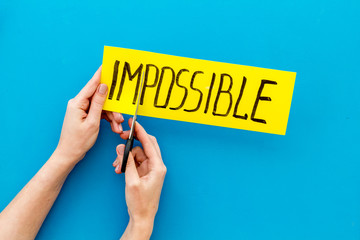 All is possible concept. Hands cut word impossible on blue background