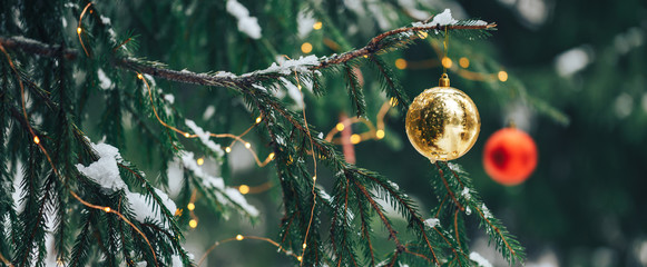Decorated Christmas tree with red and gold balls on blurred, sparkling background, outdoor.
