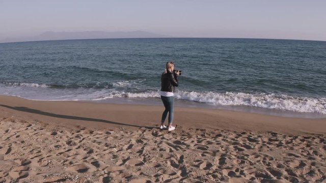 Woman photographer with DSLR camera taking pictures on empty beach during sunset.