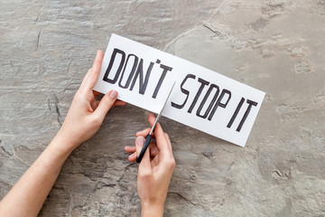 Encouragement and motivation. Hands cutting text Don't stop it with scissors on grey desk