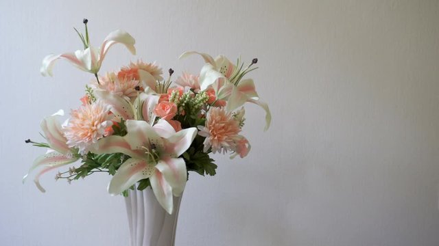 Lilies, roses, carnations flowers in pink vase on white background is rotating. Pastel flower collection presentation