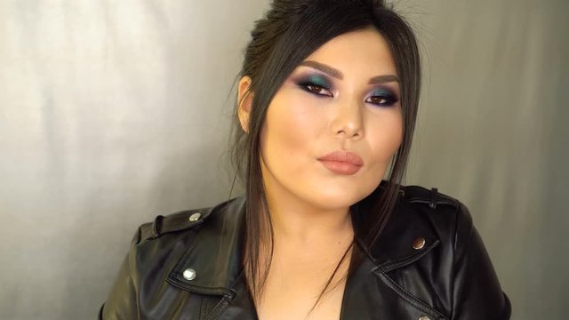 Portrait of beautiful dark haired asian model with perfect make up and stylish hairdo fishbone braid. Plus size asian model posing sitting by mirror in beauty salon. Beauty industry