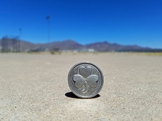 Three leaf clover silver coin balancing the ground with twin peak mountain top in the background on a sunny bright day.