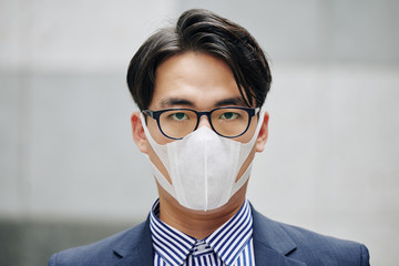 Face of serious Asian businessman wearing protective mask in city with air pollution