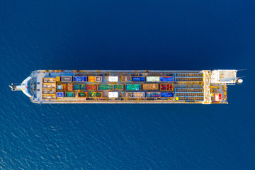 Cargo Ship loaded with colourful Containers and large crates cruising at sea, Top down aerial view.