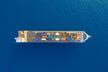Cargo Ship loaded with colourful Containers and large crates cruising at sea, Top down aerial view.