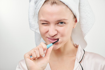 Fresh young woman with towel on head brushing her teeth in bathroom