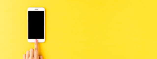 Woman’s hand using smart phone with empty screen on yellow background. Banner