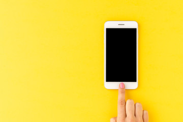 Woman’s hand using mobile phone with blank screen on yellow background. Close up
