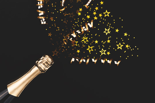 Creative New Year composition with champagne bottle and exploding gold star shape confetti. Celebration and party concept.