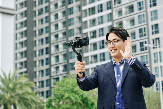 Smiling Asian businessman waving with hand when making video on smartphone for his followers - Powered by Adobe