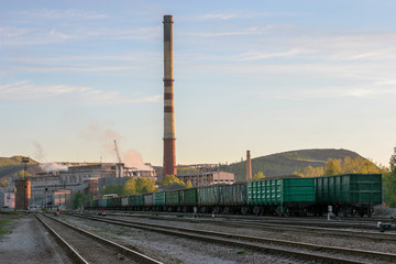 Fototapeta na wymiar Factory and many freight cars loaded with slate. High factory chimney and mountains of slate production waste. Smoke from the factory.