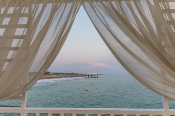 Fototapeta na wymiar beige curtain on the background of the beach of the Mediterranean Sea at sunset