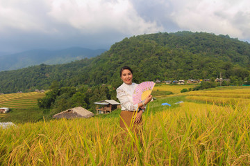 Fototapeta na wymiar A woman dressed in Lanna dress, holding folding fan in a rice field on a mountain in Pongpang forest, Mae Chaem, Chiang Mai