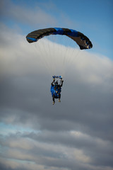 Skydiver in wingsuit under a canopy of a filled parachute on a background of blue sky with clouds close-up.