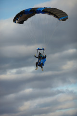 Skydiver in wingsuit under a canopy of a filled parachute against a cloudy sky close-up.