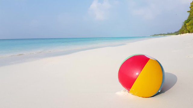 Concept design with colorful beach ball stuck on white sand of exotic beach with calm turquoise lagoon background and dusty sky in Antigua