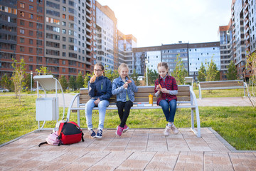 Teen girls eat on a bench in a city park.