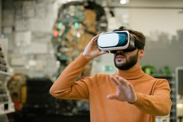 Young man in virtual reality headset stretching arm towards display