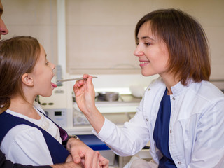 Female doctor looking at the throat of a girl patient. ENT clinic scene