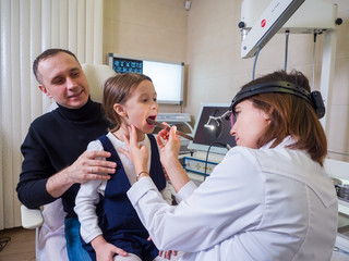 Little girl with dad at an appointment with an ENT doctor. Female doctor examines throat. Clinic scene