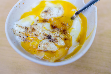 Soft boiled egg cracked open in a bowl with a hint of black pepper