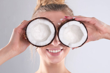 beautiful young girl with bare shoulders holds a coconut in her hands. the woman buries her eyes in...