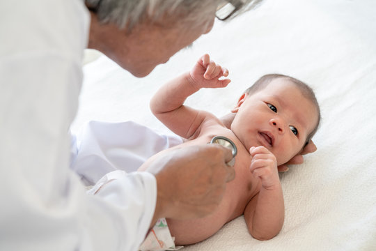 Adorable asian newborn baby girl check up examines by pediatrician doctor. Happy male doctor hand using stethoscope examining little cute baby infant heart and lung in clinic. Baby health care concept