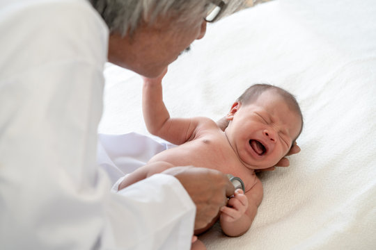 Crying asian newborn baby girl check up examines by pediatrician doctor. Happy male doctor hand using stethoscope examining little cute baby infant heart and lung in clinic. Baby health care concept.